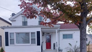 A two-story house with a red front door, number 206, and a small front yard with two potted plants. - Colorful 4-bedroom house-Vet owned-NAVAL Academy (Waukegan)