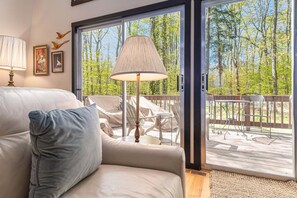 A room with a sofa, a lamp, a view through a glass door to an outdoor deck with chairs and a table. - 🏡 Sugarloaf Chalet – Pet Friendly Escape | Hot Tub • Fireplace • Loft • Bar Area ➠ 2510 (Cedar)
