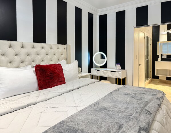 Une chambre à coucher avec une tête de lit capitonnée, un miroir rond, une table de chevet blanche et un plaid gris.