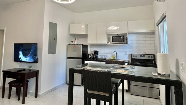 A modern kitchen with white cabinets, a microwave, a stove, and a dining area with a table and chairs. - Cozy studio #2 in Venetian Road (Venetian Road Settlement)