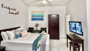 A hotel room with a bed, a desk, a TV, a wardrobe, and a ceiling fan. - Cozy studio #2 in Venetian Road (Venetian Road Settlement)