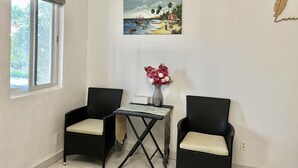 A room with two wicker chairs, a small table with a vase of flowers, and a painting of a beach scene on the wall. - Cozy studio #2 in Venetian Road (Venetian Road Settlement)