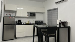 A modern kitchen with white cabinets, a built-in microwave, a refrigerator, a dining table with chairs, and a ceiling light fixture. - Cozy studio #2 in Venetian Road (Venetian Road Settlement)
