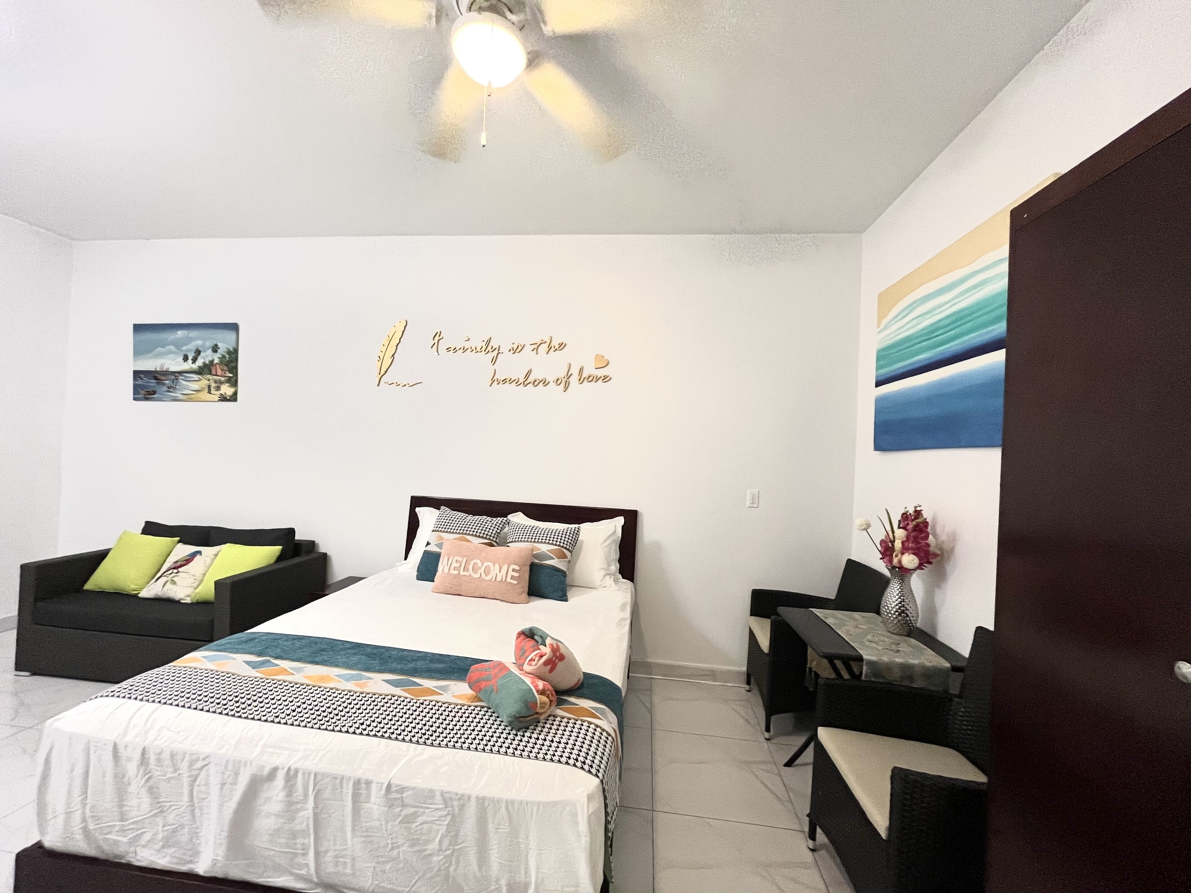 Une chambre à coucher comprenant un lit, un bureau, une chaise, un ventilateur de plafond et un mur orné d’une citation décorative.