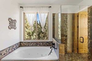 Un bagno con una vasca da bagno ampia, una zona doccia e una finestra con tende.