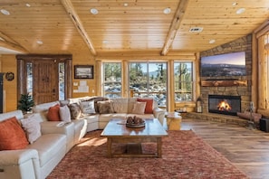 A cozy living room with a stone fireplace, a large window overlooking a scenic view, and a comfortable seating area.