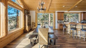 Un interno spazioso in legno, con zona pranzo, cucina e ampie finestre che offrono vista sugli alberi.