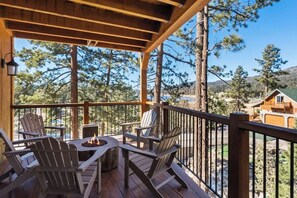 Un patio in legno con poltrone Adirondack, un braciere e vista su alberi e colline circostanti.