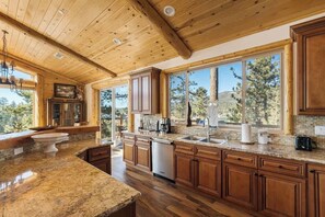 Cucina spaziosa con mobili in legno, piani di lavoro in granito e ampie finestre che si affacciano su alberi e colline.
