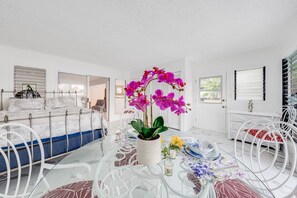 Relax in a bright and airy room with a neatly made bed, glass dining table, and a potted plant.
