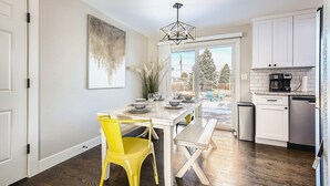Una cocina con armarios blancos, una mesa de comedor con sillas amarillas y vistas al exterior.