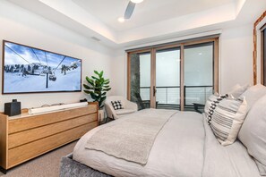Une chambre avec un lit, une commode, une grande fenêtre et une image représentant un paysage de ski accrochée au mur.