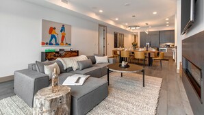 Ein modernes Wohnzimmer mit grauem Sofa, einem Couchtisch und einem Essbereich mit Holztisch und Stühlen.