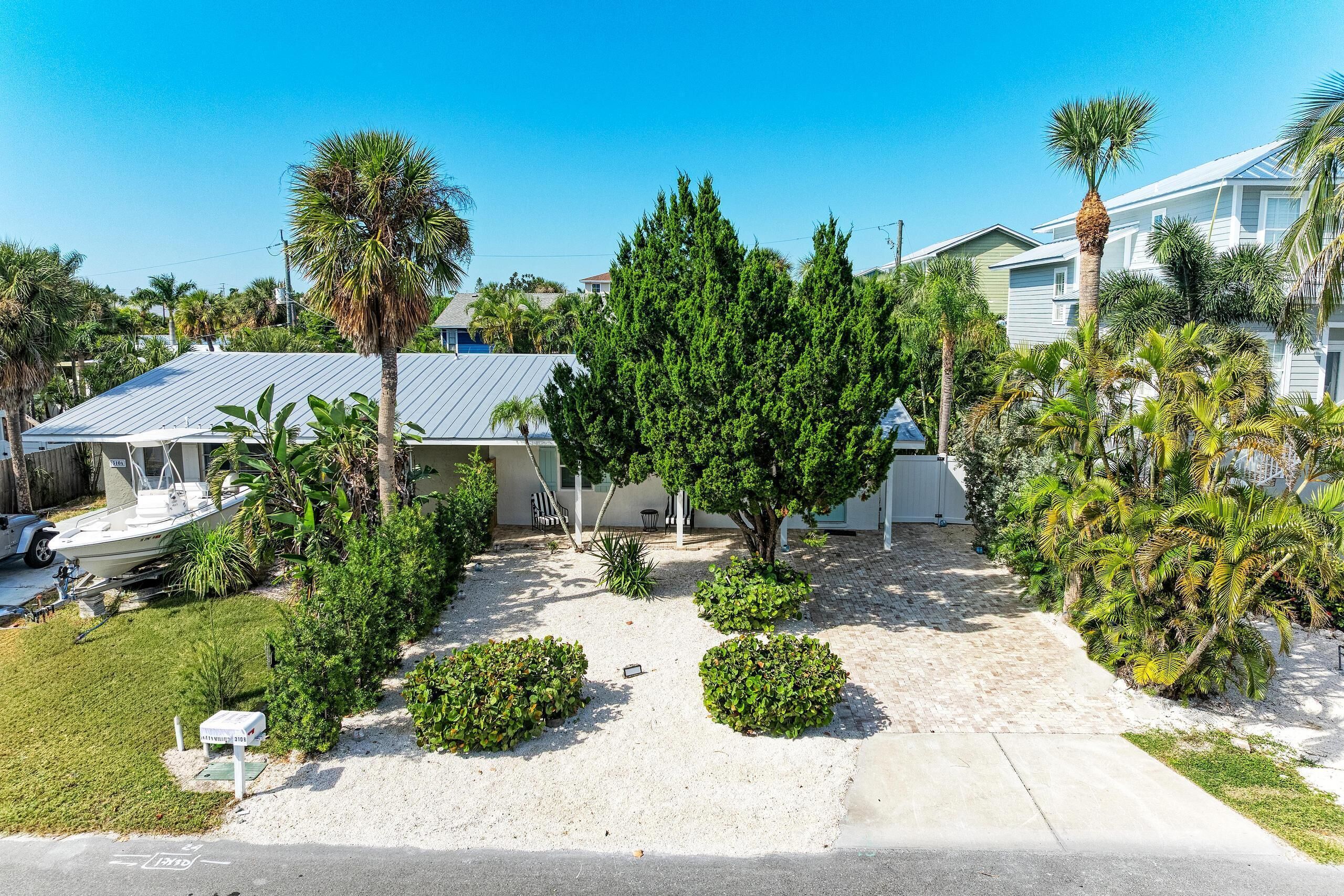 A residential area with a house featuring a metal roof, surrounded by palm trees and other greenery.