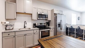 A modern kitchen with white cabinets, stainless steel appliances, a wooden dining table, and a bar area with stools. - Silver Reef Mine | Ball Pit & Hot Tub (Hurricane)