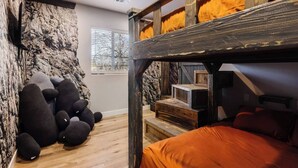 A bunk bed with a wooden frame and orange bedding, a stone wall, and a window with blinds. - Silver Reef Mine | Ball Pit & Hot Tub (Hurricane)