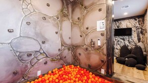 A room with a stone wall design, a ball pit filled with orange and red balls, and a seating area with dark cushions. - Silver Reef Mine | Ball Pit & Hot Tub (Hurricane)