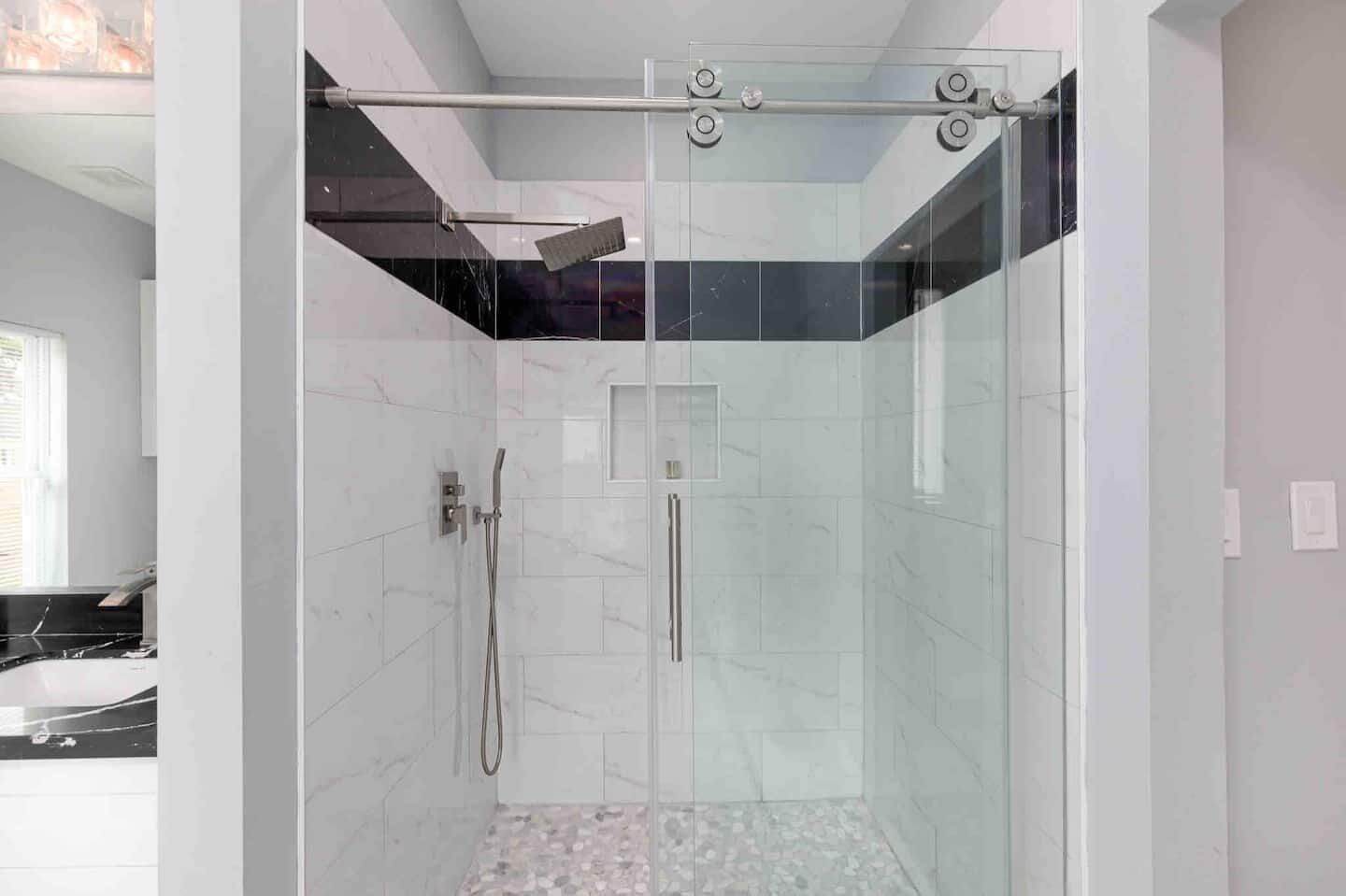 A modern shower with a glass door, a handheld showerhead, and a pull-down rain shower head.