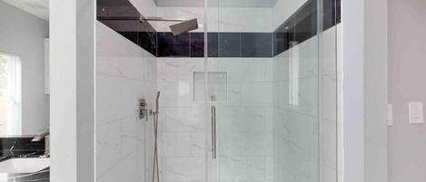 A modern shower with a glass door, a handheld showerhead, and a pull-down rain shower head.