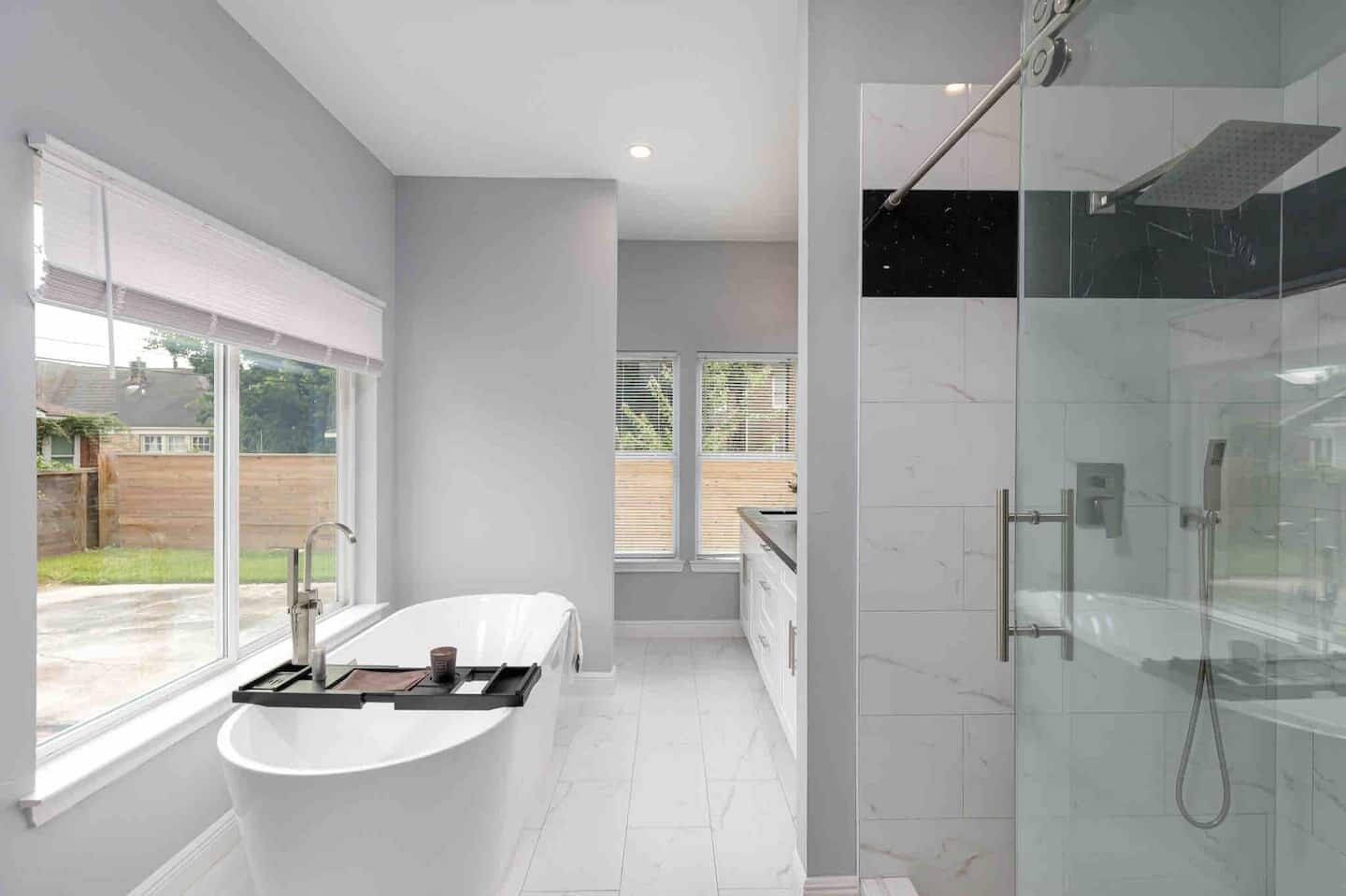 A modern bathroom with a freestanding bathtub, a glass-enclosed shower, and a large window providing a view of the outdoors.