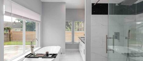 A modern bathroom with a freestanding bathtub, a glass-enclosed shower, and a large window providing a view of the outdoors.