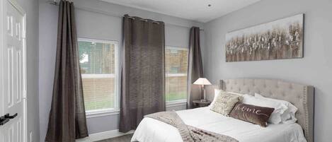 A bedroom with a bed, curtains, a ceiling fan, a window with blinds, and a painting on the wall.