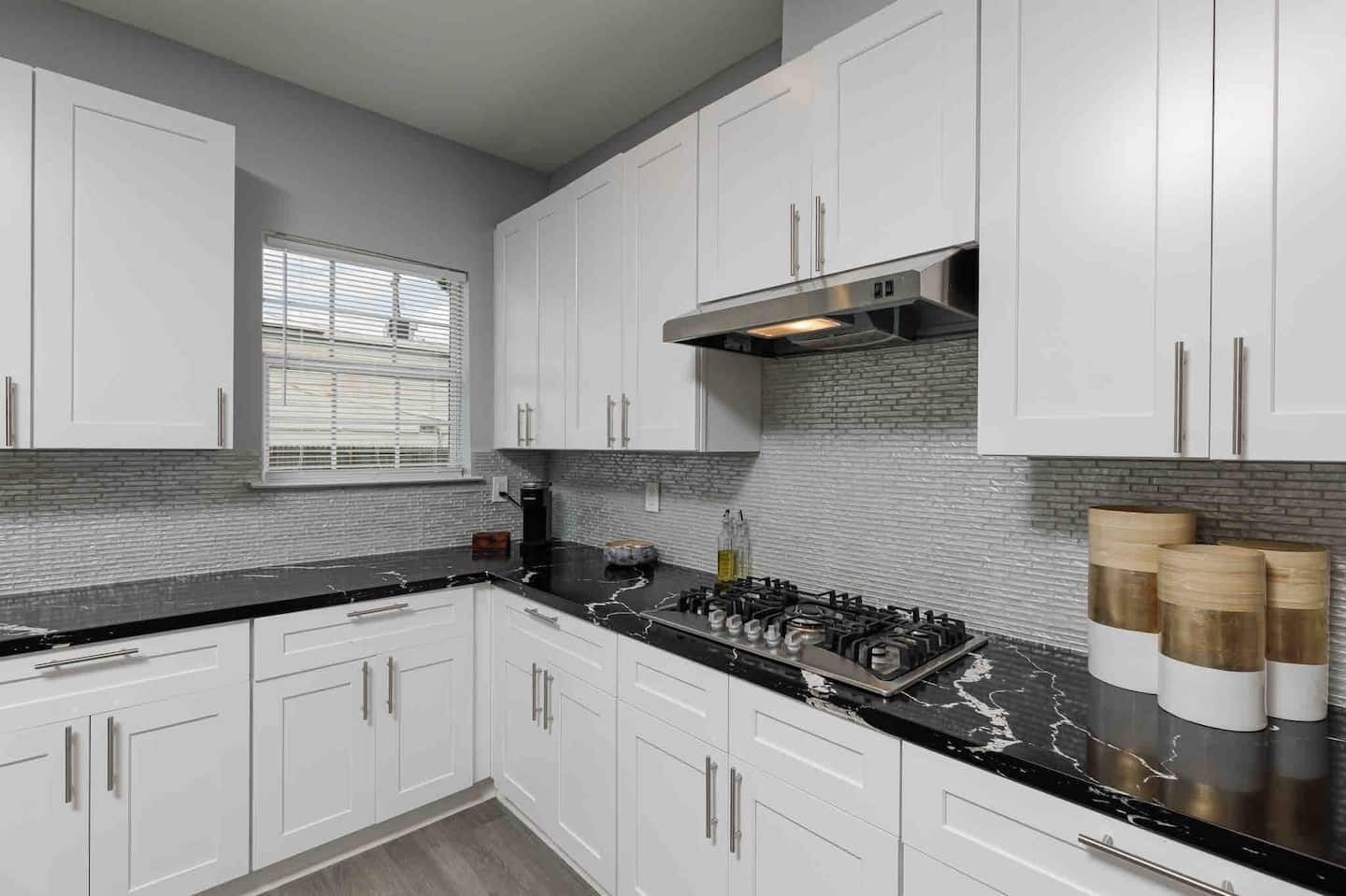A modern kitchen with white cabinets, a black countertop, and a stainless steel range hood.