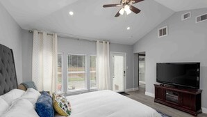 Ein Schlafzimmer mit einem großen Bett, einem Fernseher auf einem Holztisch und einem Deckenventilator.