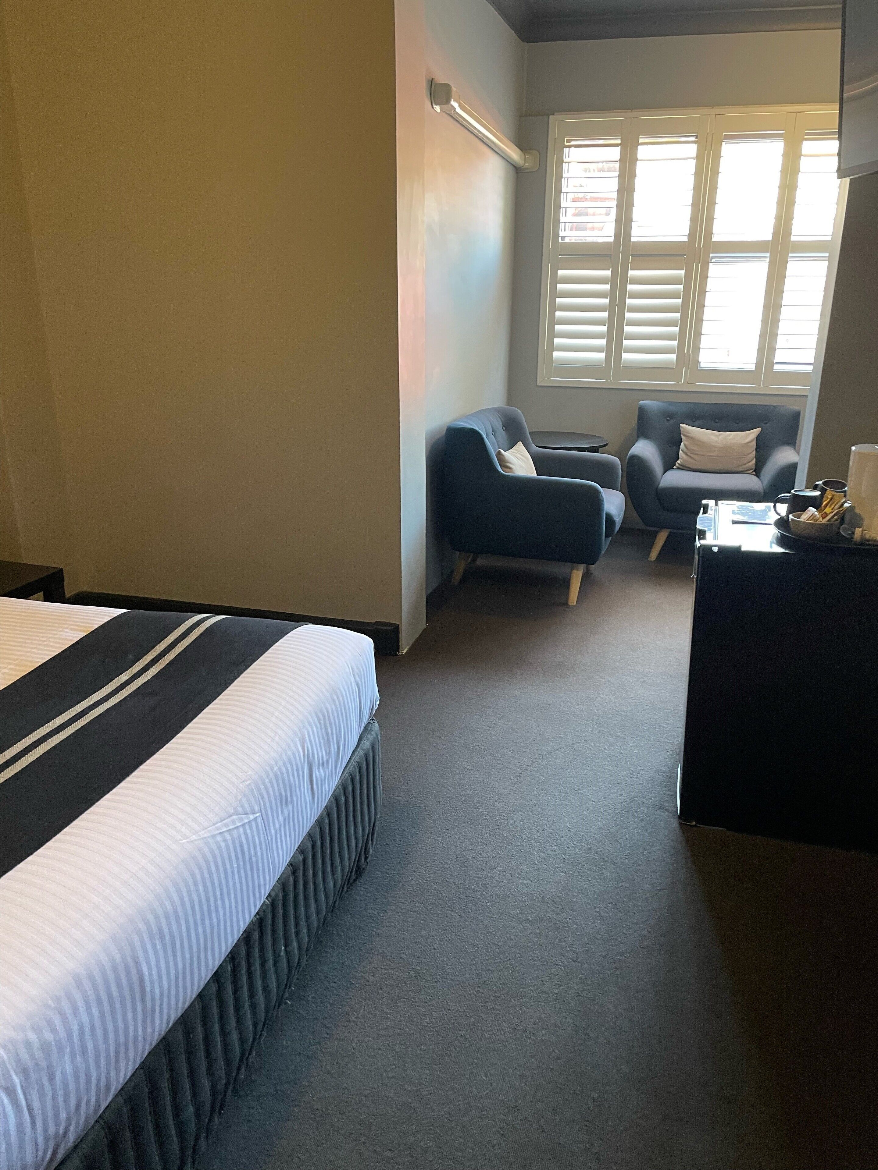 A hotel room with a bed, two armchairs, a small table, and a window with blinds.