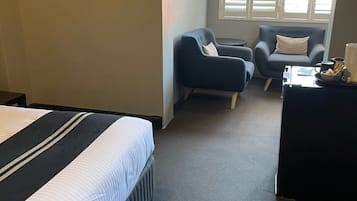 Een hotelkamer met een bed, twee fauteuils, een bijzettafeltje en een raam met jaloezieën.