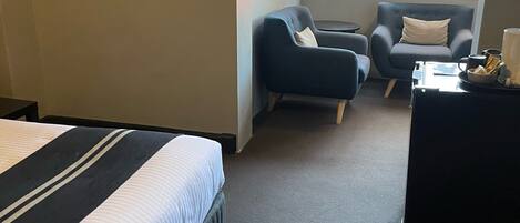 A hotel room with a bed, two armchairs, a small table, and a window with blinds.
