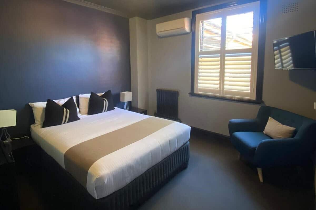 A hotel room with a large bed, a desk, a chair, an air conditioning unit, and a television on the wall.