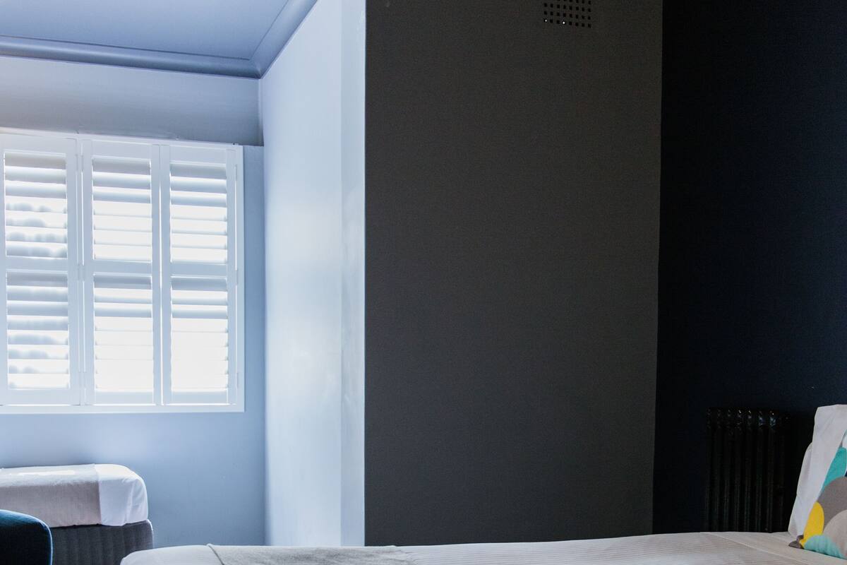A bedroom with a bed, a chair, and a window with shutters.