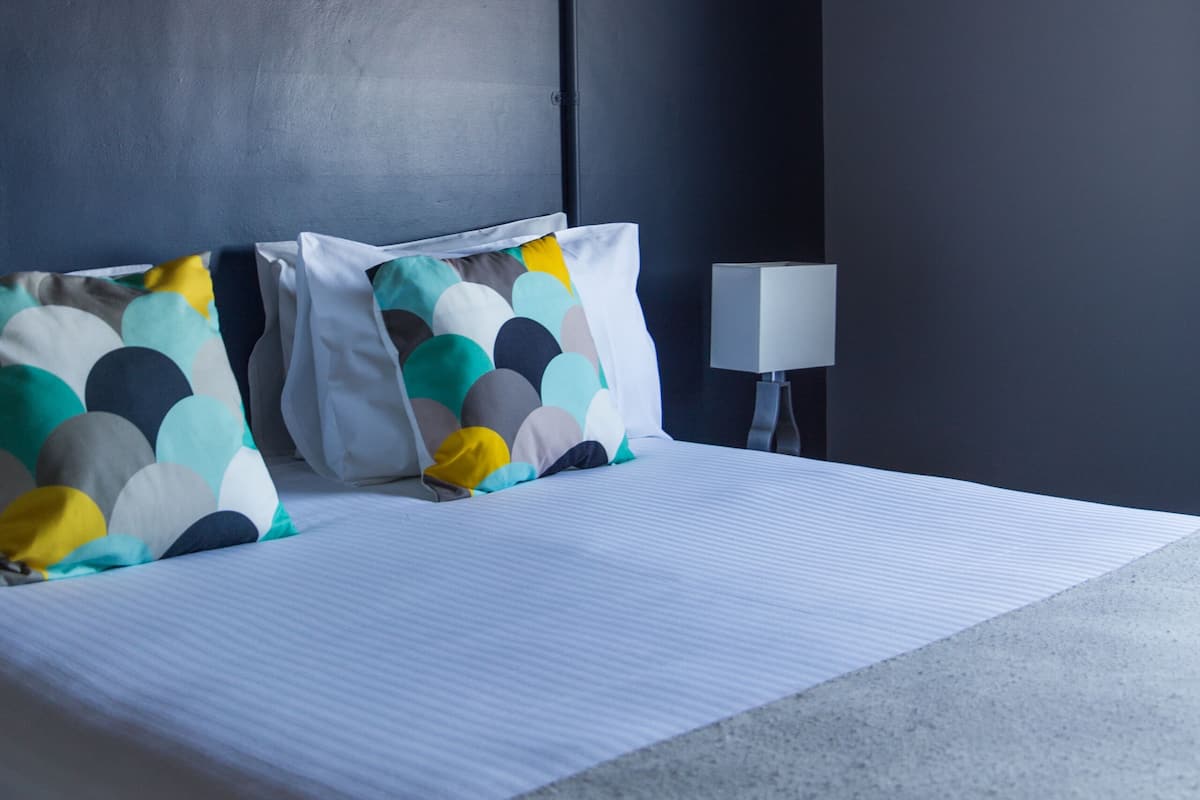 A hotel room with a bed, pillows, a lamp, and an air conditioning unit.