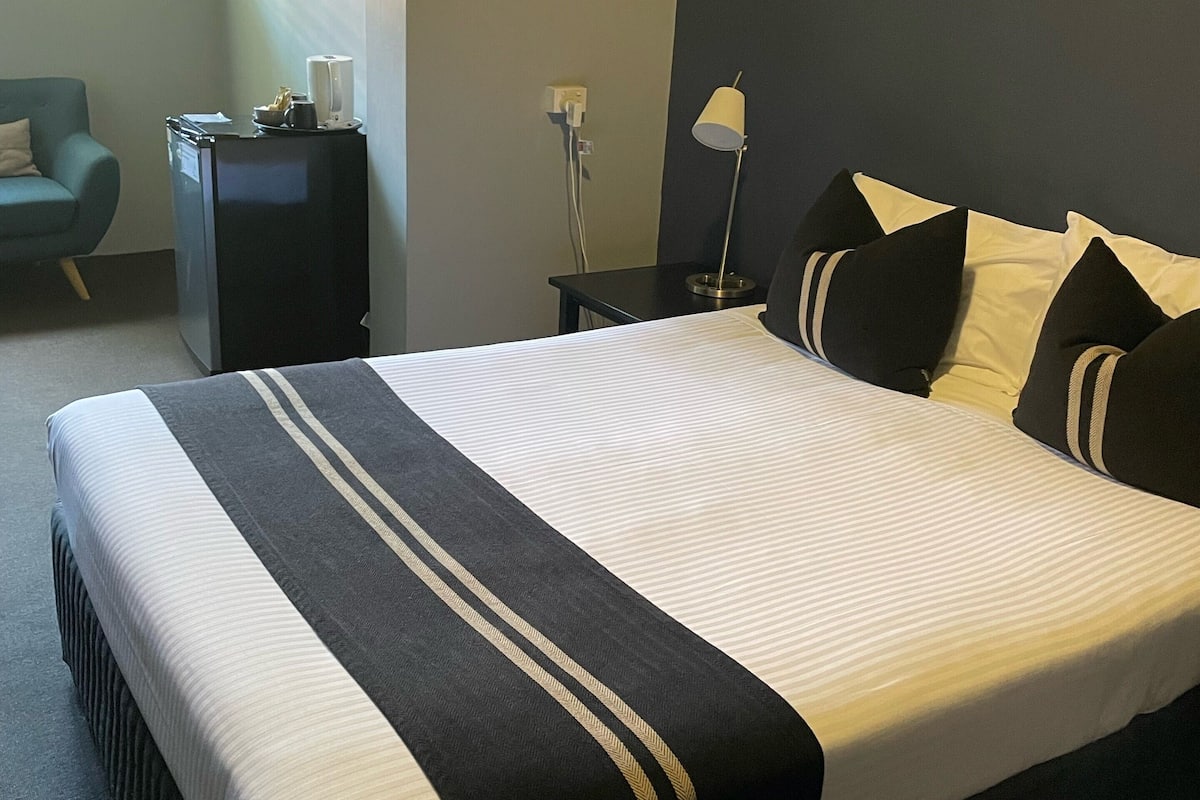 A hotel room with a large bed, a desk, a chair, and a lamp.