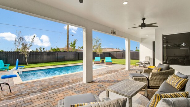 A covered outdoor area with a pool, patio furniture, and a view of the backyard. - Sea Turtle Retreat - Luxurious 4 Bedroom/2 Bath, Electric Heated Pool with Fenced in Yard (Cape Coral)