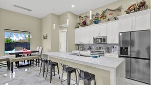 A modern kitchen with white cabinets, stainless steel appliances, and a large island with bar stools. - Sea Turtle Retreat - Luxurious 4 Bedroom/2 Bath, Electric Heated Pool with Fenced in Yard (Cape Coral)