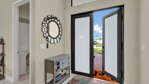 A hallway with a door leading outside, a mirror on the wall, and a small cabinet with drawers. - Sea Turtle Retreat - Luxurious 4 Bedroom/2 Bath, Electric Heated Pool with Fenced in Yard (Cape Coral)