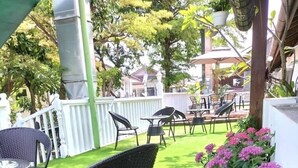 An outdoor patio area with artificial grass, wicker furniture, and pink flowering plants. - Le meilleur (George Town)