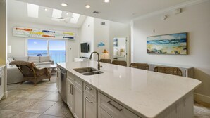 A modern kitchen with a large island, a dining area with wicker chairs, and a view of the ocean.