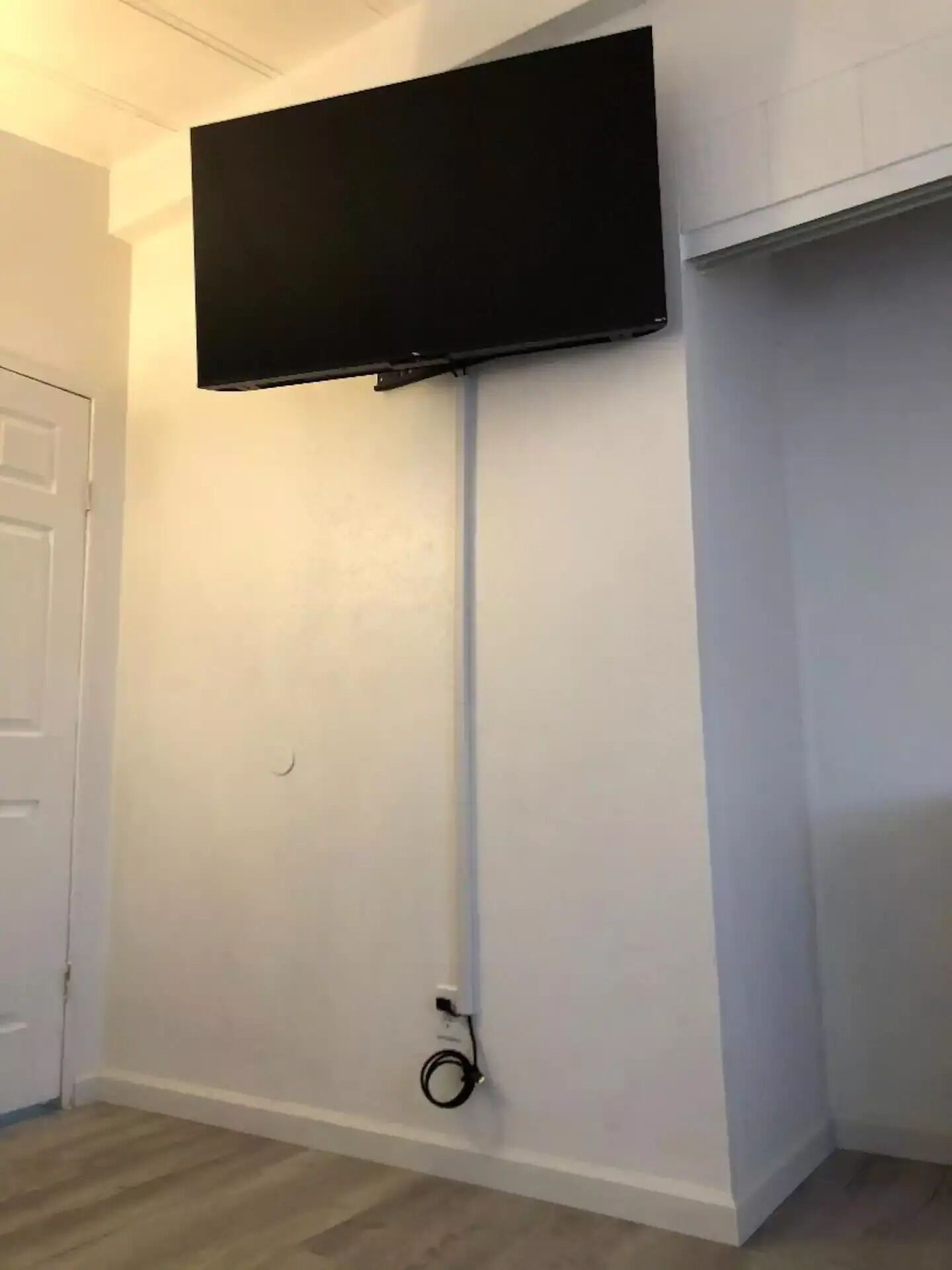 Quarto com televisão de tela plana fixada na parede, porta branca e carpete claro.