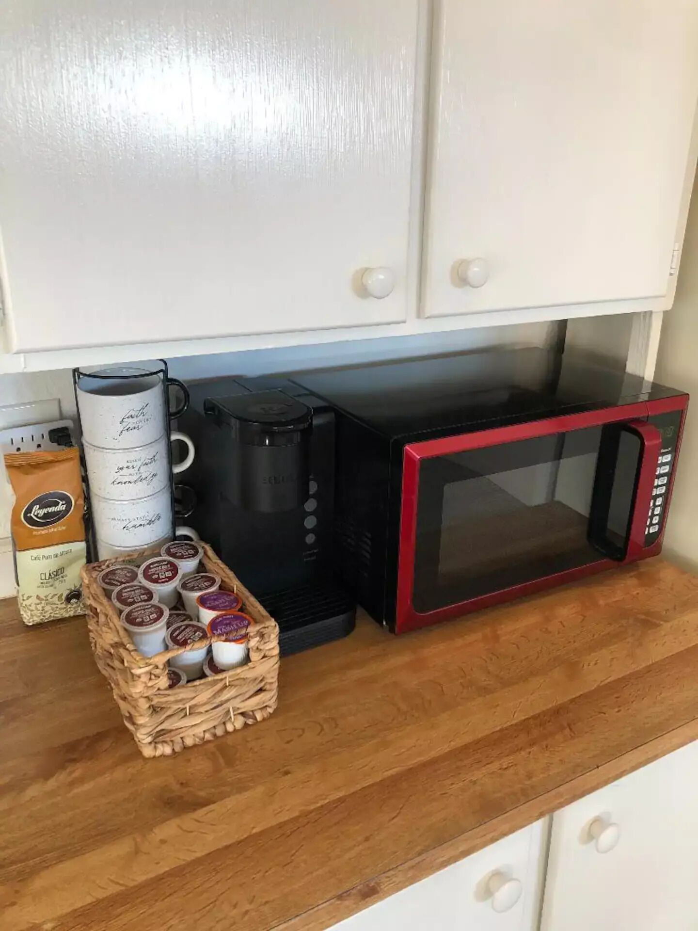 A kitchen with a coffee maker, a red microwave, and a basket of coffee pods.