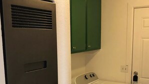 A laundry room with a washer and dryer, green cabinets above, and a white door. - The Green River House (Bullhead City)