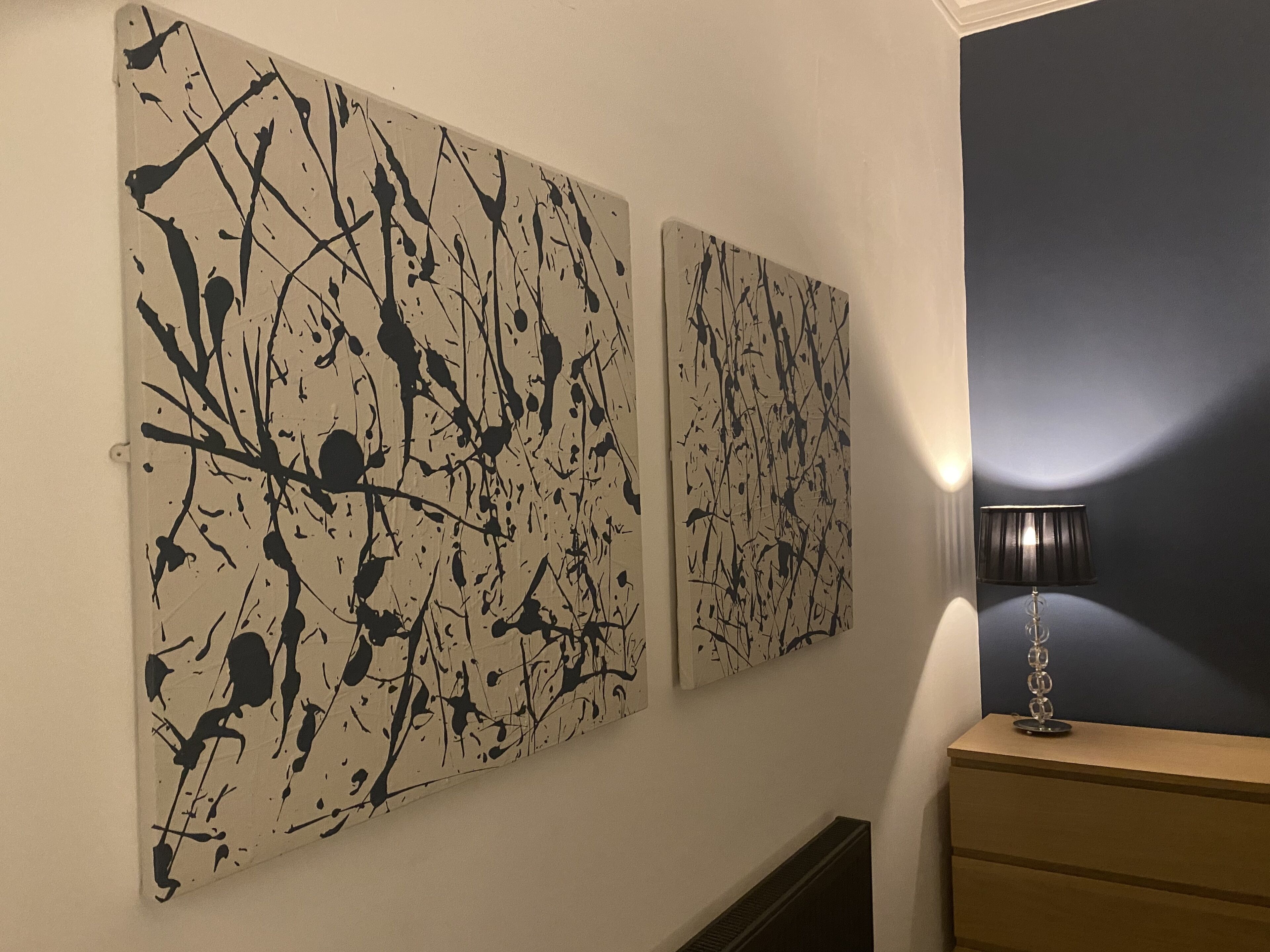 Dos grandes cuadros abstractos en una pared, una lámpara y un aparador de madera.
