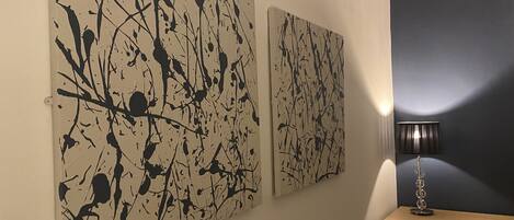 Dos grandes cuadros abstractos en una pared, una lámpara y un aparador de madera.