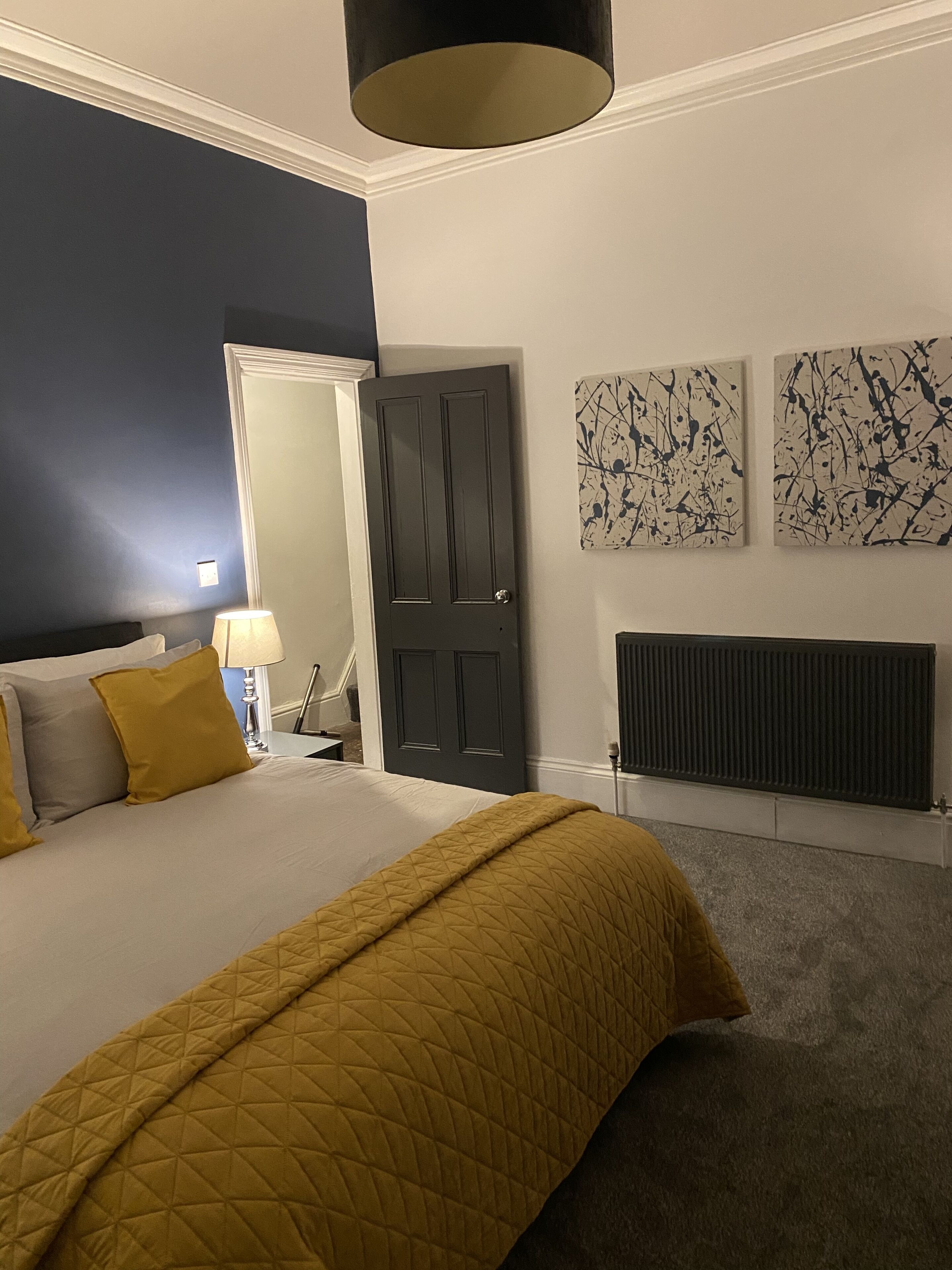 Un dormitorio con cama, una puerta, un radiador y dos cuadros abstractos en la pared.