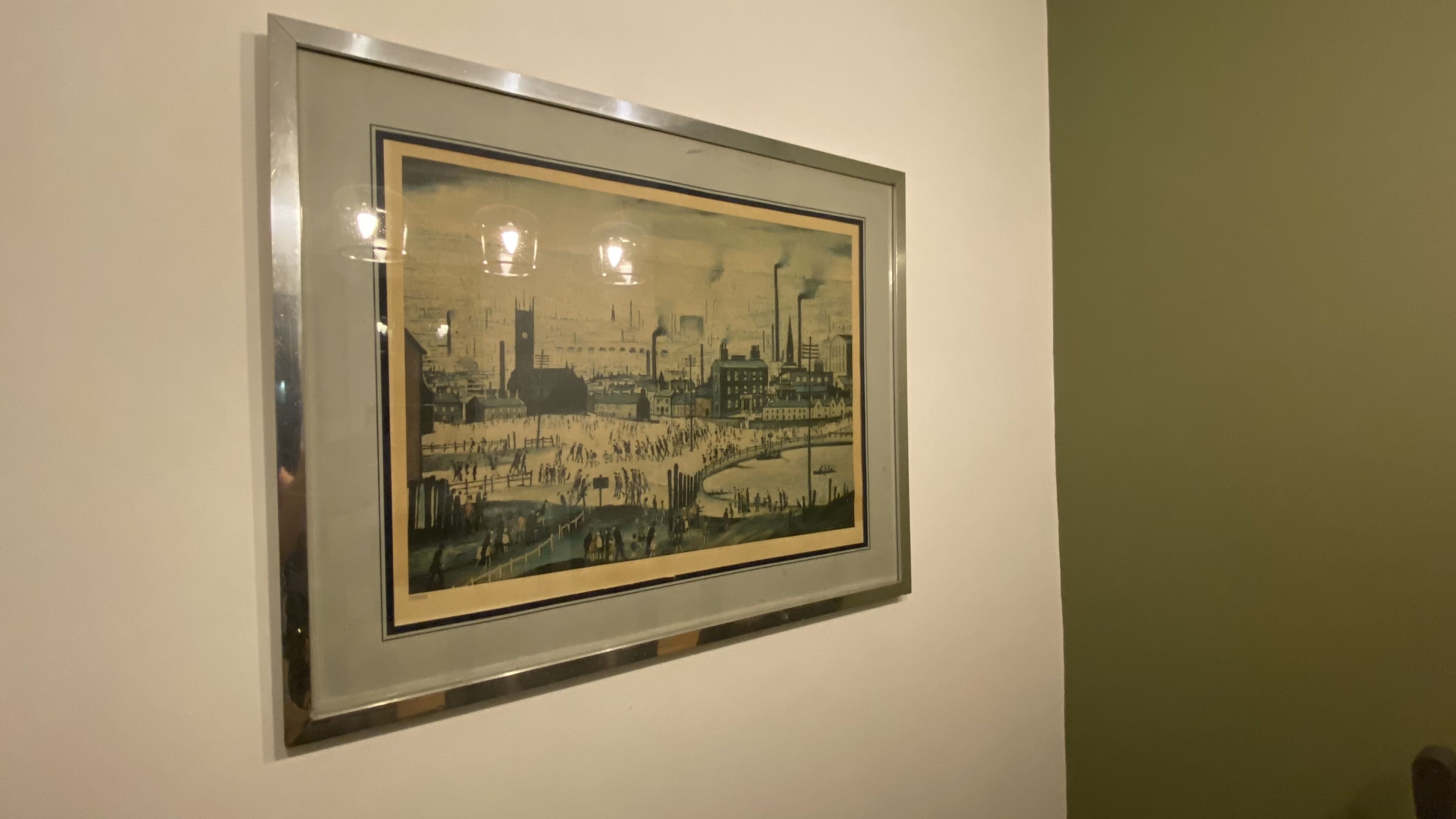 Un tableau historique encadré représentant une scène industrielle animée, avec des bâtiments, des cheminées d’usine et une rivière.