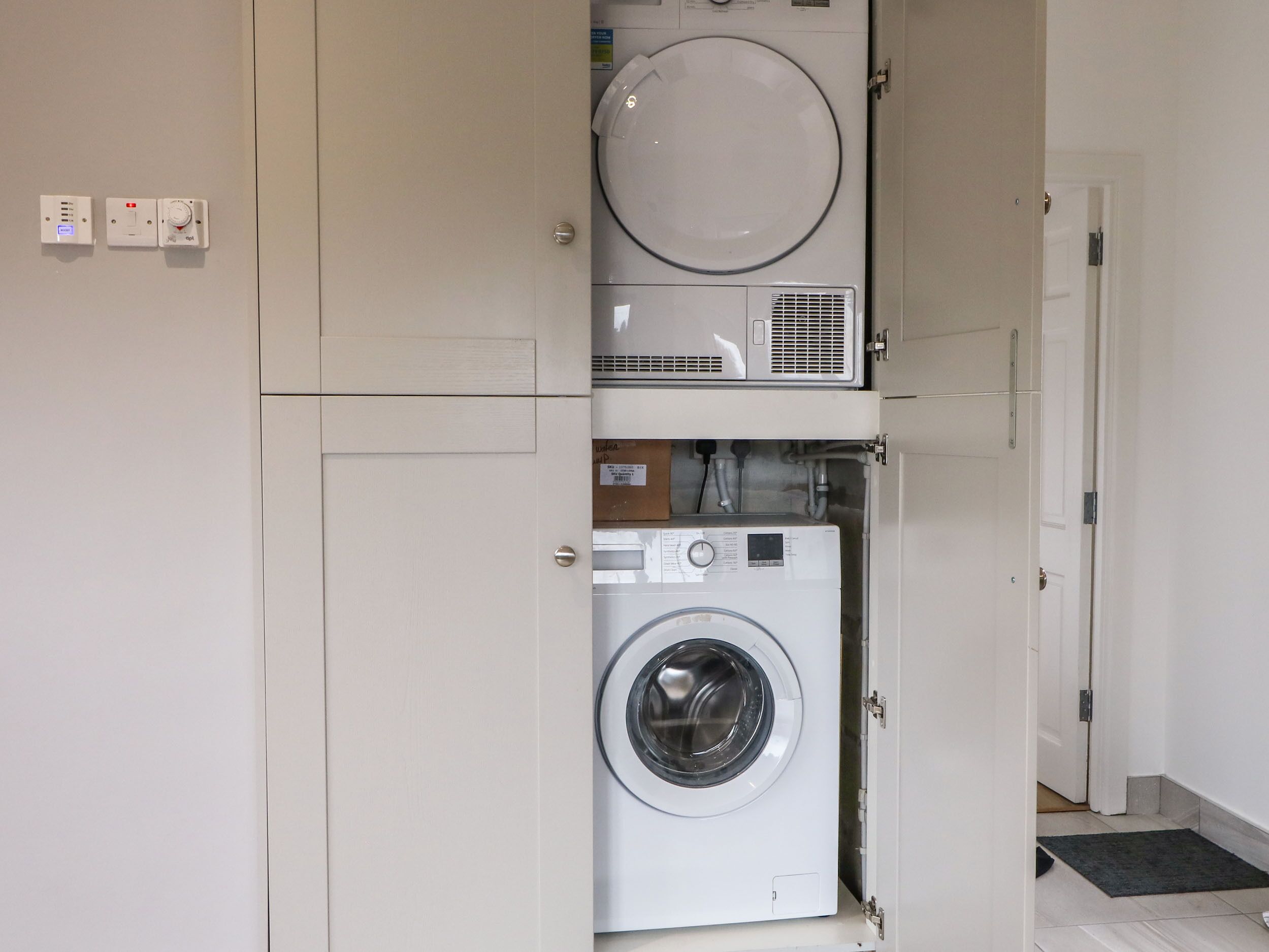 Uma lavanderia compacta com máquina de lavar de abertura superior e secadora de abertura frontal, ambos em branco, num espaço pequeno com uma porta que dá para outro quarto.