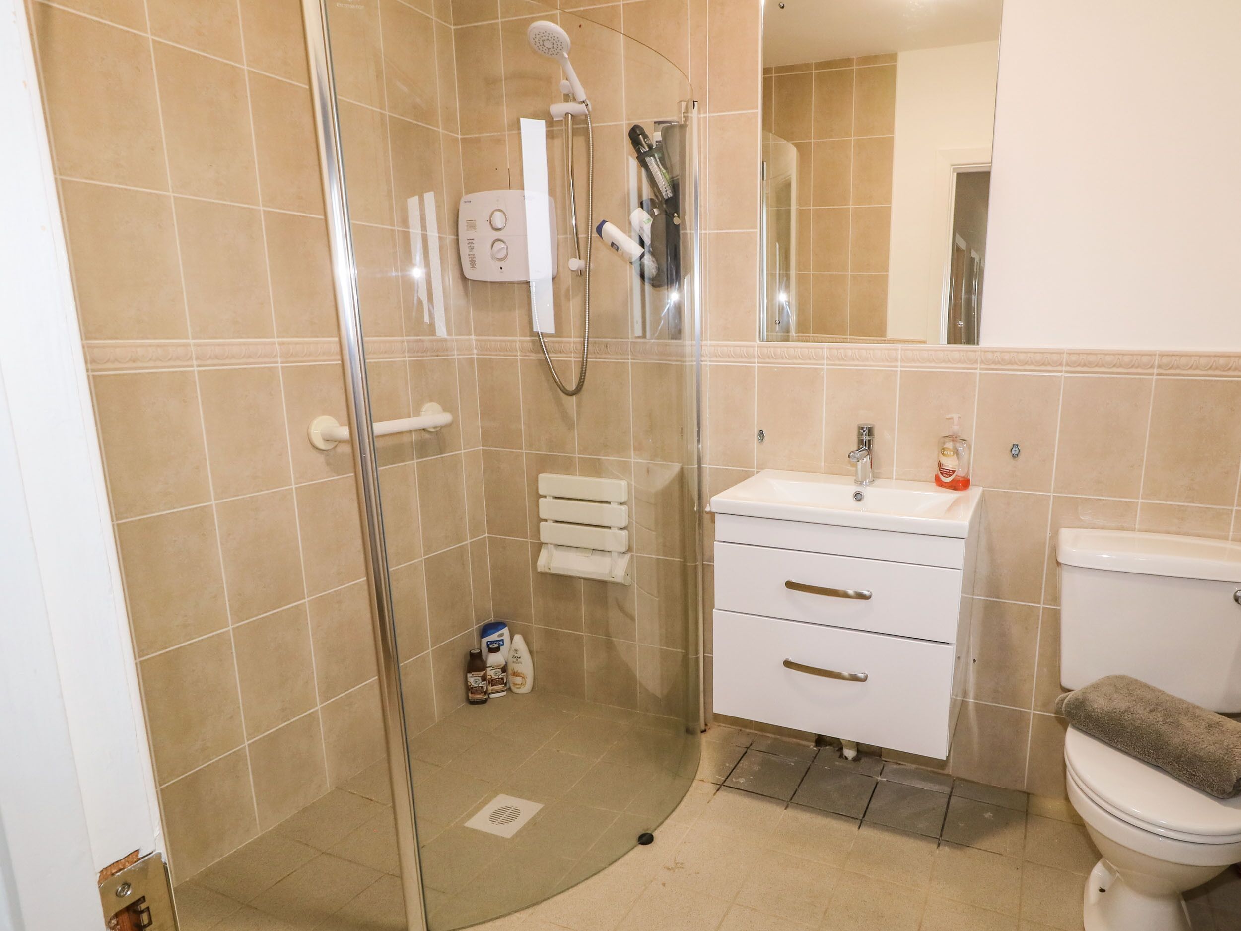 Un baño con cabina de ducha de vidrio, un lavamanos blanco con espejo y un inodoro.