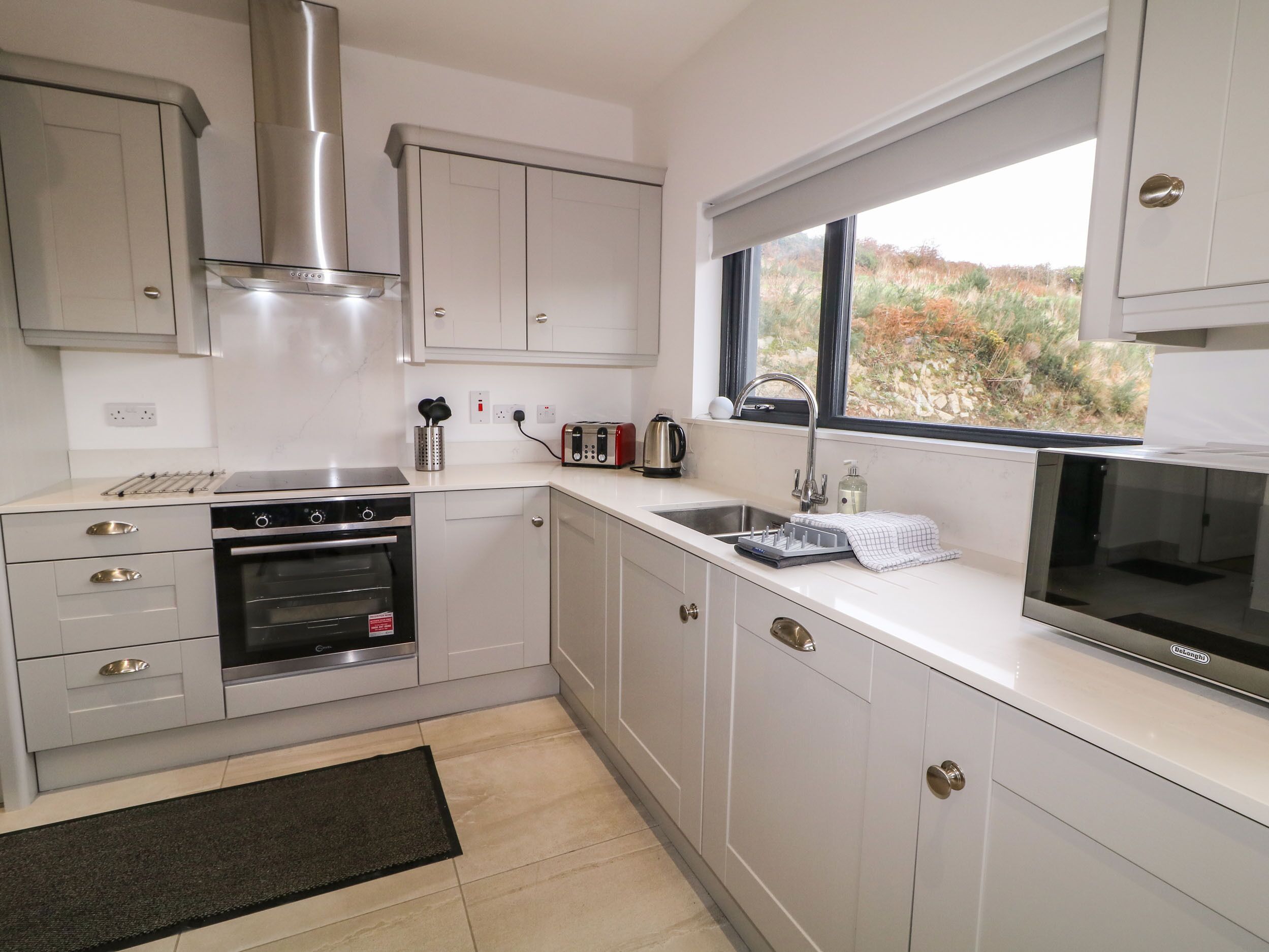 A modern kitchen with white cabinetry, a built-in oven, a stainless steel range hood, a double sink, and a window with a view of the outdoors.
